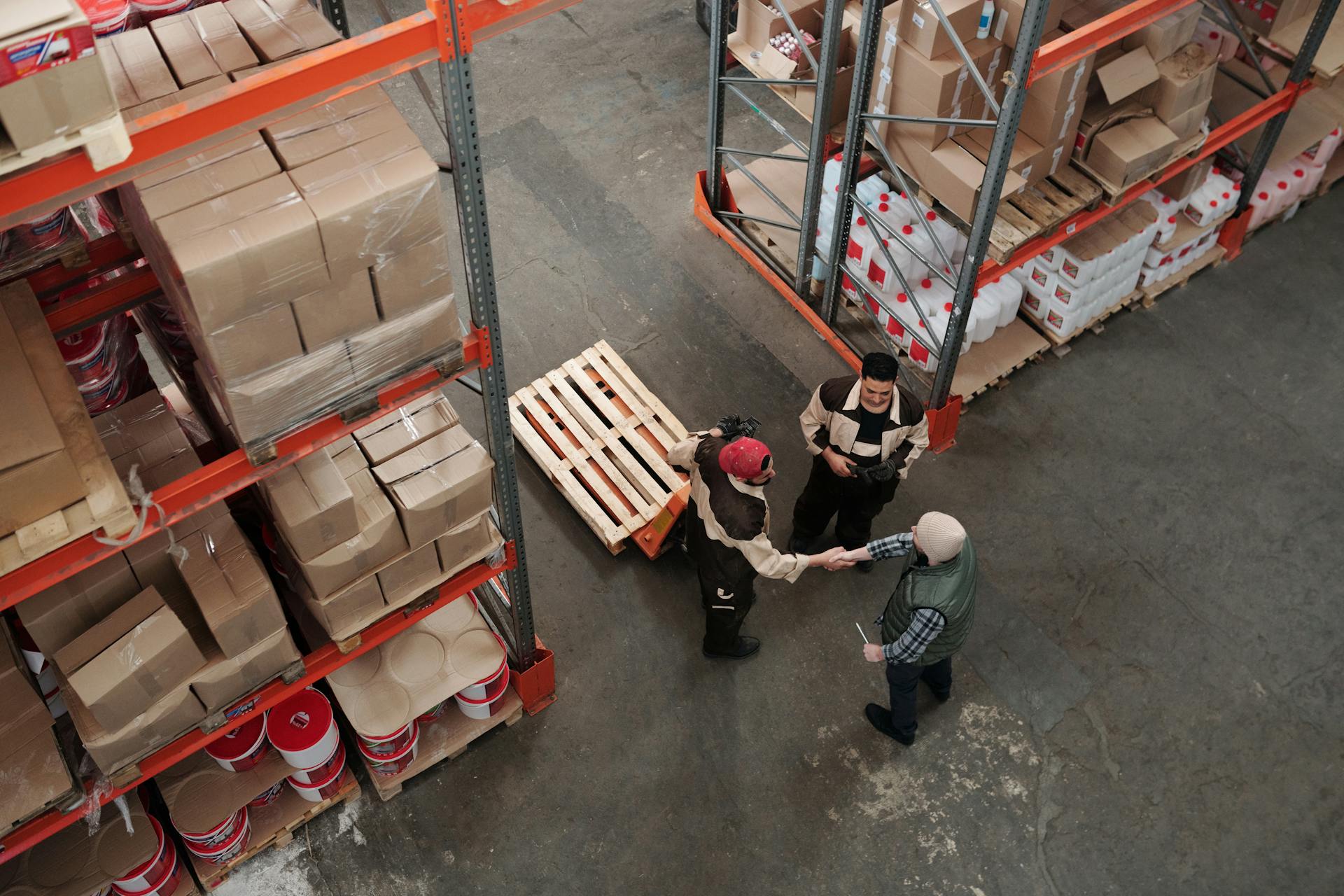High‑angle view of two business partners shaking hands inside a busy warehouse, representing product sourcing